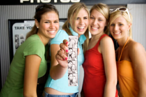 Four teenage girls (16-18) holding photo booth pictures, portrait
